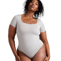 Woman wearing a light gray bodysuit against a white background